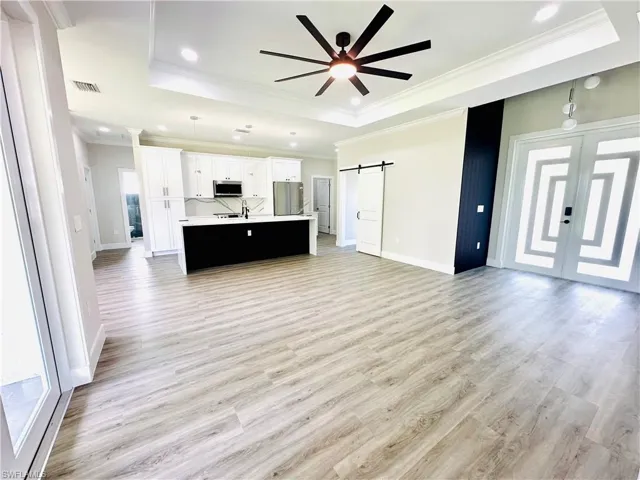 Unfurnished living room featuring a barn door, crown molding, light wood-style flooring, a raised ceiling, and french doors