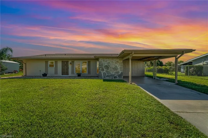 View of front of property featuring driveway, stone siding, a carport, and covered porch