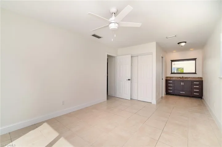 Unfurnished bedroom featuring light tile patterned floors, ceiling fan, a closet, and ensuite bathroom
