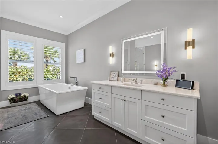 Primary Bathroom featuring vanity, a soaking tub, dark tile patterned flooring, a marble finish shower, and crown molding