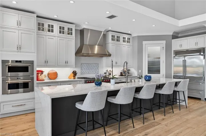 Kitchen with light stone counters, recessed lighting, a kitchen breakfast bar, stainless steel appliances, and a large island with sink