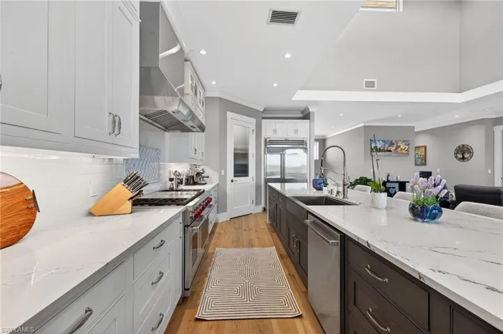 Kitchen featuring light stone counters, high quality appliances, light wood finished floors, two tone cabinetry, and recessed lighting