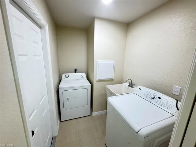Dedicated laundry area featuring a utility sink with a chrome faucet, light-toned wall finishes, and light-colored tile flooring