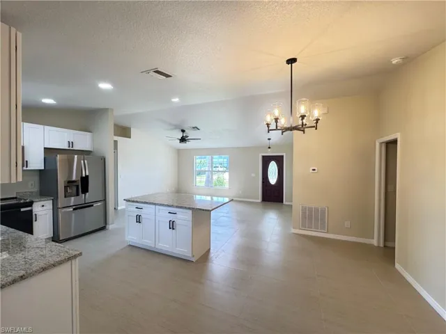 Open-concept living space featuring a central kitchen island with granite countertops, recessed lighting, a modern chandelier, and tile flooring throughout