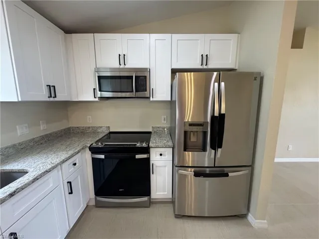 Contemporary kitchen featuring white shaker cabinetry, granite countertops, stainless steel appliances, and light-toned tile flooring