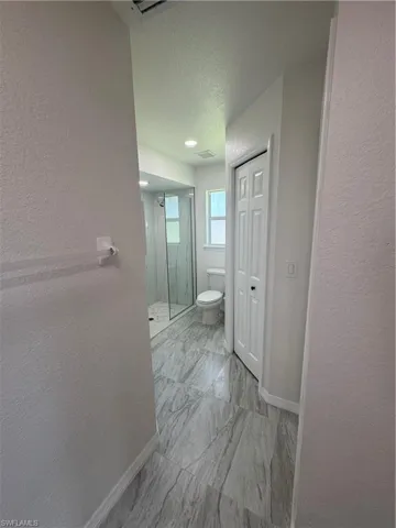 Bathroom featuring large format gray patterned tile flooring, a glass-enclosed shower with white tiled floor, and a window providing natural light