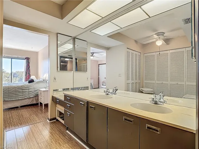 Ensuite bathroom featuring double vanity, light wood-style floors, ceiling fan, and a closet