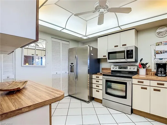 Kitchen with stainless steel appliances, white cabinetry, a ceiling fan, wooden counters, and light tile patterned floors