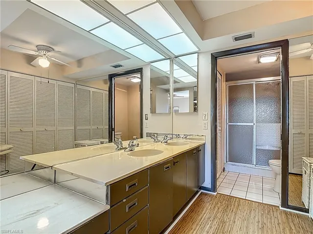 Bathroom with a closet, double vanity, ceiling fan, a shower stall, and light wood-type flooring