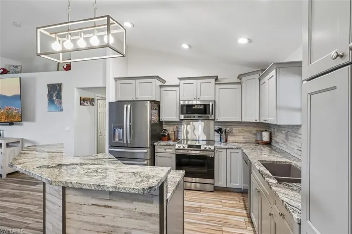 Kitchen featuring light wood-finish flooring, light gray cabinetry, stainless steel appliances, and a U-shaped island with a marbled countertop