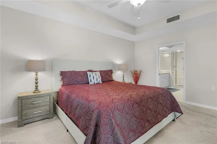 Bedroom with ceiling fan, light colored carpet, and ensuite bath
