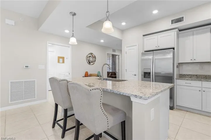 Kitchen featuring white cabinetry, stainless steel fridge, an island with sink, and pendant lighting