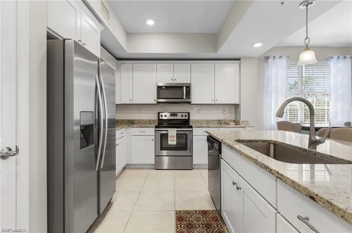 Kitchen with appliances with stainless steel finishes, light stone counters, sink, white cabinets, and light tile patterned flooring