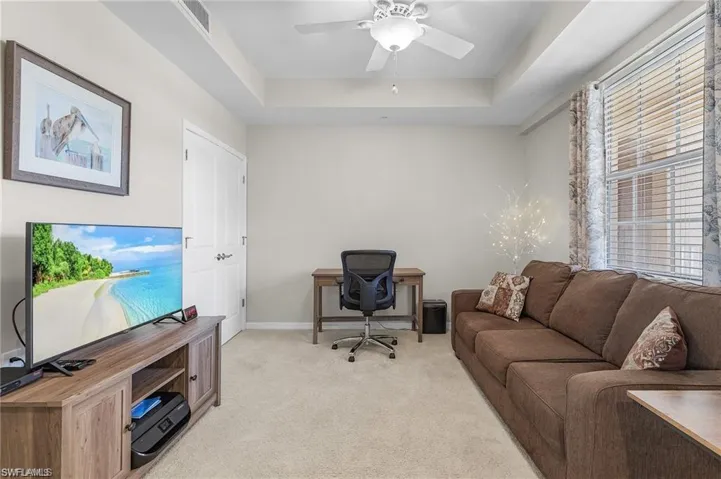 Office area featuring ceiling fan, light carpet, and a tray ceiling