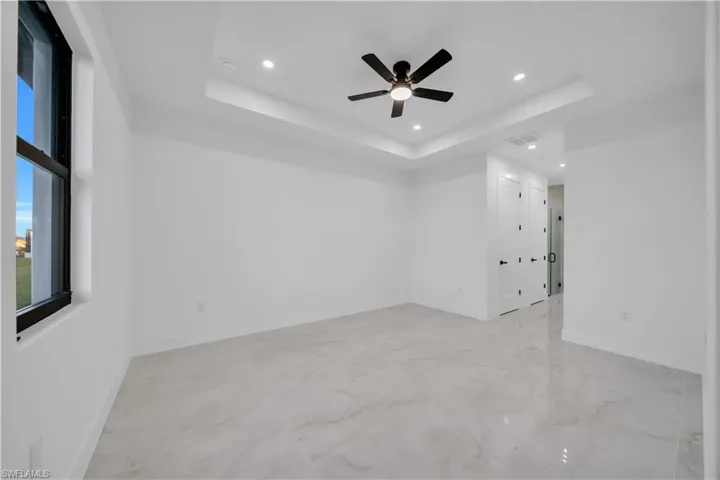 Unfurnished room with a tray ceiling, recessed lighting, light marble finish floors, and a ceiling fan