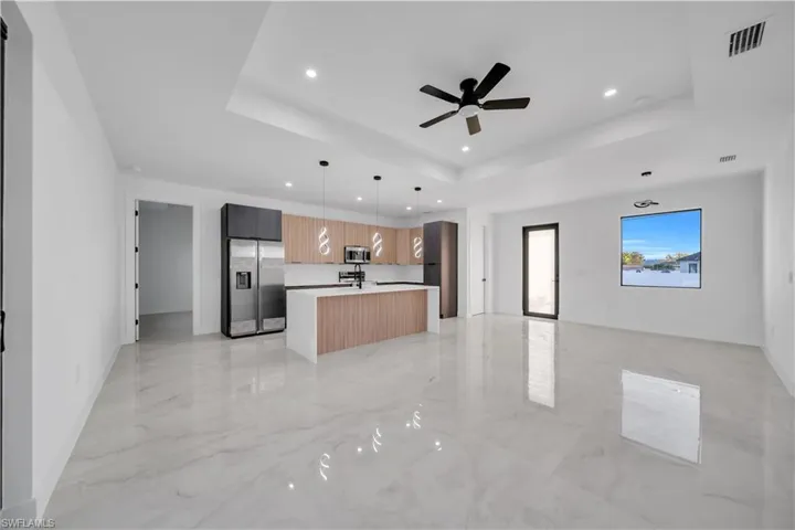 Kitchen featuring open floor plan, modern cabinets, appliances with stainless steel finishes, decorative light fixtures, and light marble finish floors