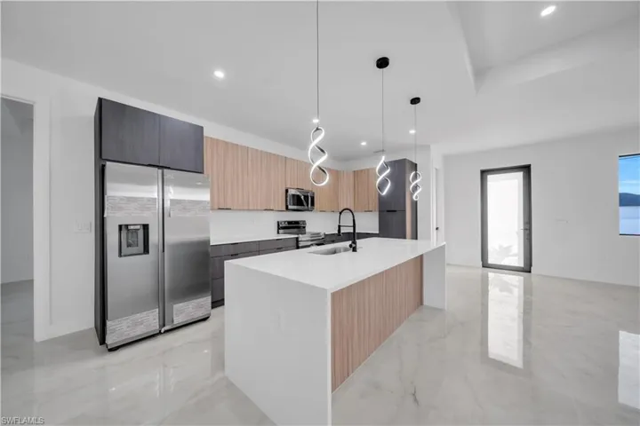 Kitchen featuring stainless steel appliances, modern cabinets, light stone counters, light brown cabinetry, and pendant lighting