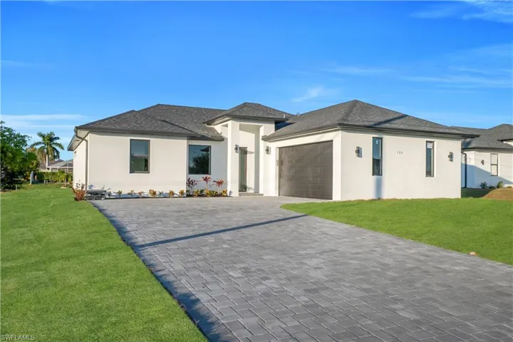 Prairie-style house with a front yard, stucco siding, decorative driveway, and an attached garage