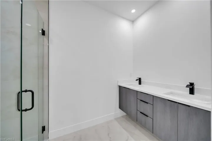 Bathroom with double vanity, light marble finish flooring, a marble finish shower, and recessed lighting