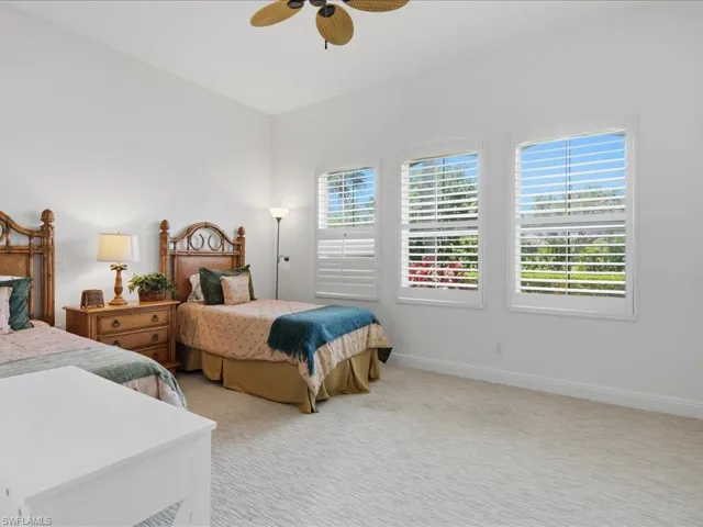 Spacious room featuring three arched windows with white plantation shutters, a vaulted ceiling, a ceiling fan, and light-toned patterned carpeting