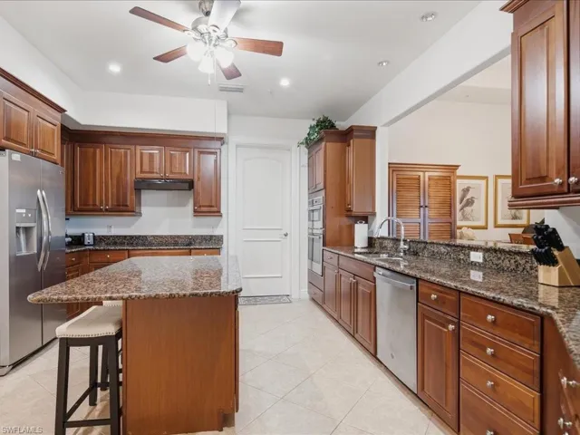Kitchen featuring wood cabinetry, stainless steel appliances, a center island with seating, granite countertops, and recessed lighting