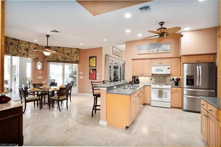 Kitchen featuring kitchen peninsula, a kitchen breakfast bar, ceiling fan, appliances, and light marble flooring.