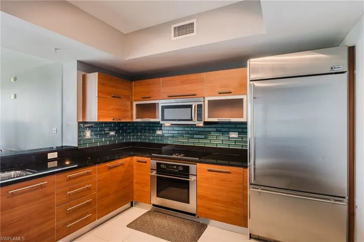Two tone kitchen featuring stainless steel appliances, light tile patterned floors, dark stone countertops, decorative backsplash, and dual tone cabinetry
