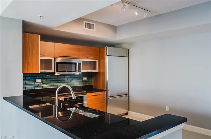 Kitchen featuring wood finish cabinetry, stainless steel appliances, a peninsula, dark stone counters, and rail lighting