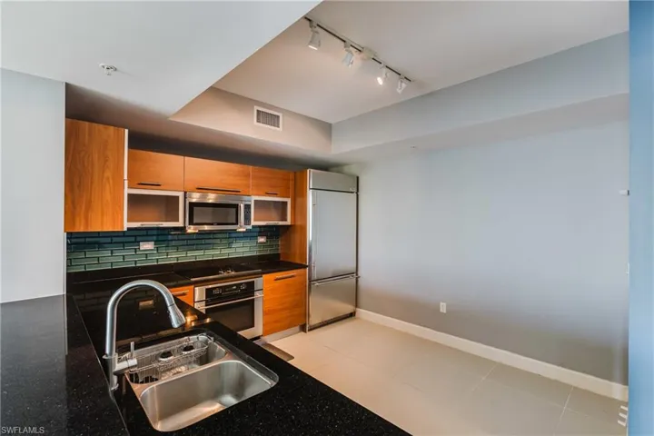 Kitchen with rail lighting, wood finish cabinets, stainless steel appliances, light tile patterned floors, and a raised ceiling
