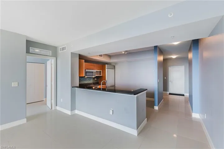 Kitchen featuring wood finish cabinetry, backsplash, a peninsula, light tile patterned flooring, and stainless steel microwave