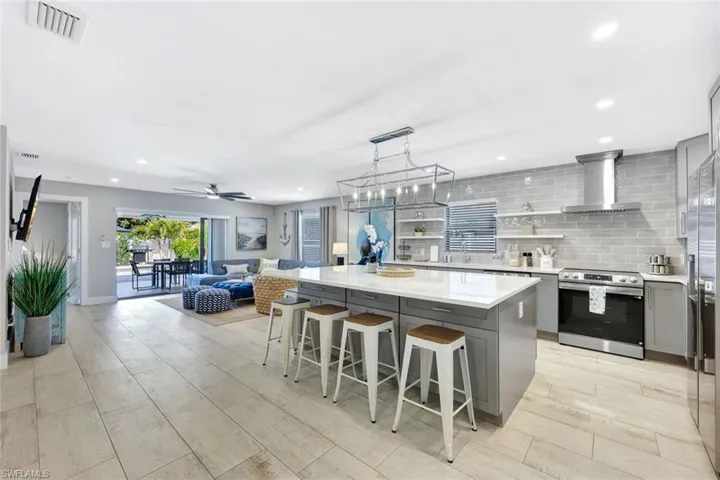 Kitchen with gray cabinetry, a breakfast bar, stainless steel appliances, tasteful backsplash, and open shelves