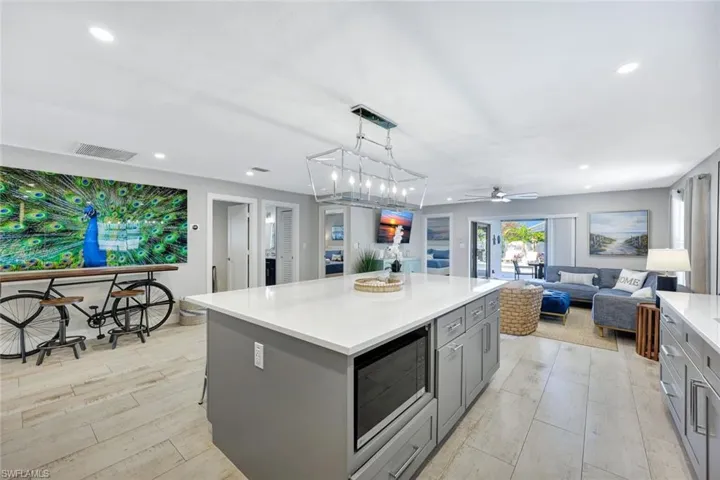 Kitchen featuring gray cabinetry, a center island, decorative light fixtures, open floor plan, and stainless steel microwave