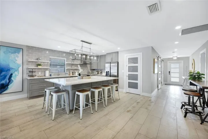 Kitchen featuring gray cabinets, a breakfast bar, decorative backsplash, light stone countertops, and a center island