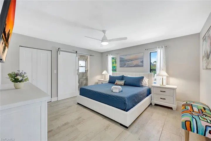 Bedroom featuring a barn door, a closet, light wood-type flooring, ensuite bathroom, and ceiling fan