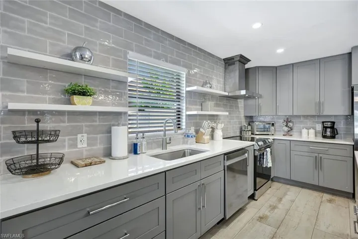 Kitchen with open shelves, gray cabinets, light stone countertops, stainless steel appliances, and recessed lighting