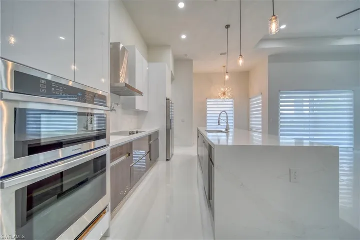 Kitchen with modern cabinets, wall chimney exhaust hood, stainless steel appliances, a sink, and white cabinets