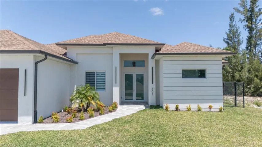 Rear view of property featuring a yard, stucco siding, a shingled roof, french doors, and an attached garage