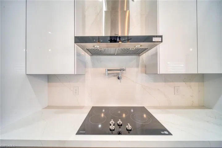 Kitchen with black electric cooktop, white cabinetry, modern cabinets, wall chimney range hood, and tasteful backsplash