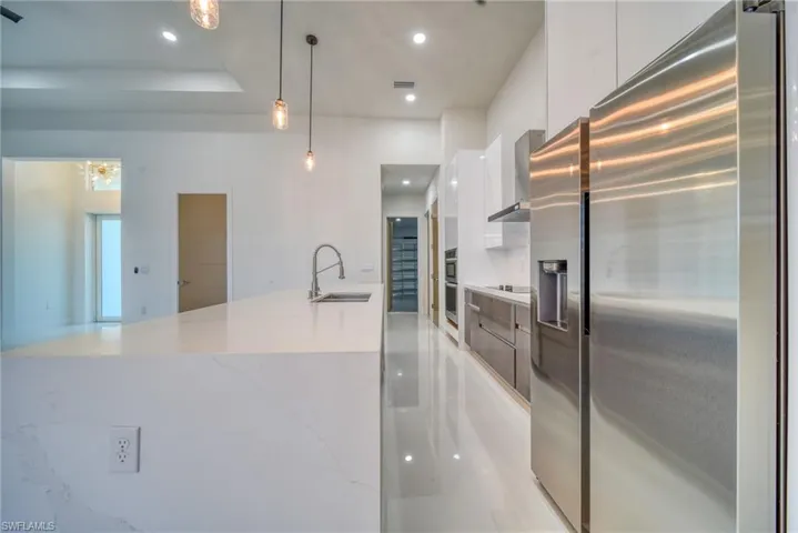 Kitchen featuring modern cabinets, stainless steel appliances, a sink, white cabinets, and wall chimney range hood