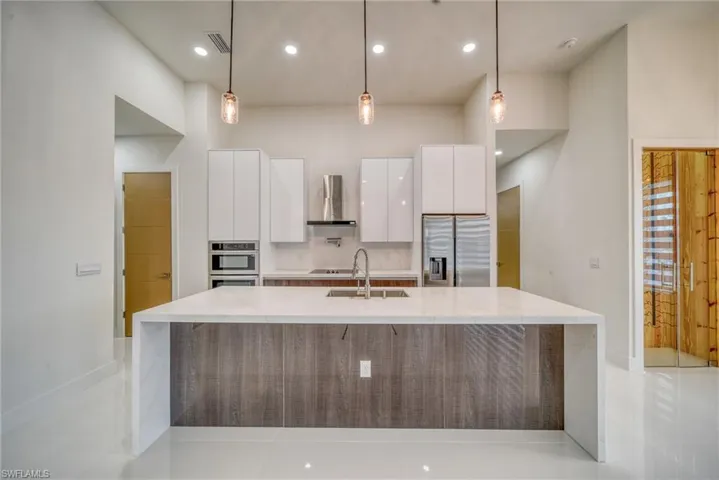 Kitchen with stainless steel fridge with ice dispenser, modern cabinets, wall chimney exhaust hood, a sink, and white cabinetry