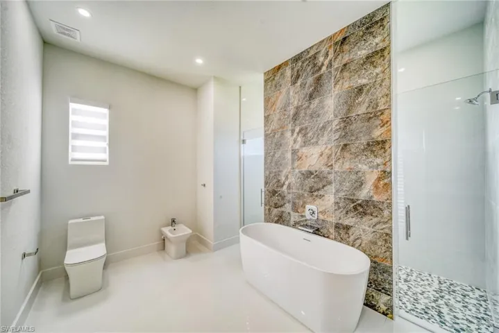 Full bathroom featuring tile walls, toilet, a shower stall, a freestanding bath, and a bidet