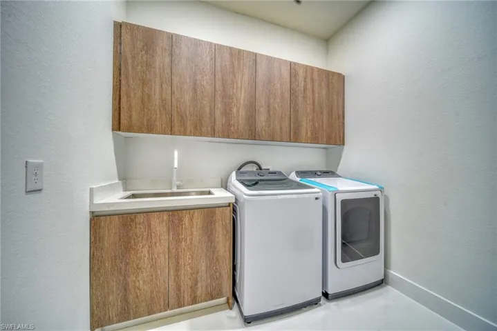 Laundry room with cabinet space, washer and dryer, a textured wall, and baseboards
