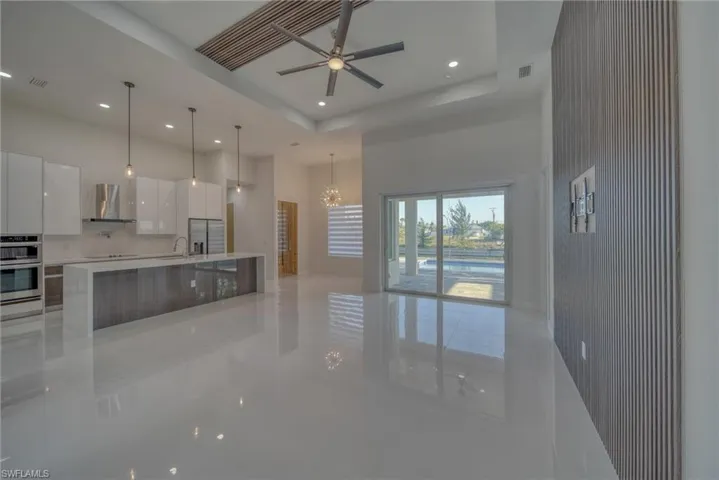 Kitchen featuring modern cabinets, light tile patterned flooring, a towering ceiling, a sink, and wall chimney exhaust hood