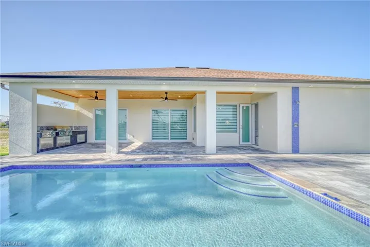 Back of property with an outdoor kitchen, ceiling fan, stucco siding, a patio, and an outdoor pool