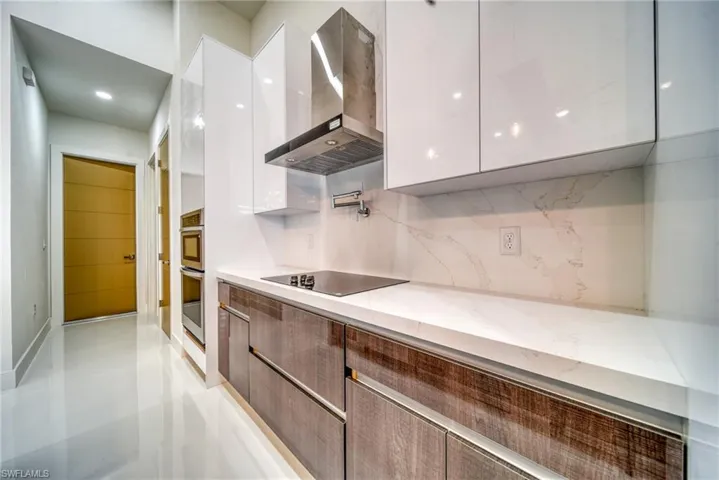 Kitchen with modern cabinets, wall chimney exhaust hood, white cabinets, black electric stovetop, and backsplash