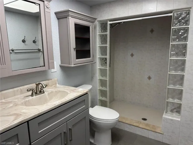 Full bathroom with vanity, dual sink a textured wall, a shower stall, and light tile patterned floors