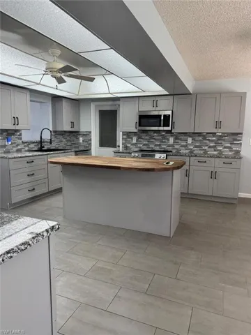 Kitchen with gray cabinetry, a kitchen island, ceiling fan, stainless steel appliances, and tasteful backsplash