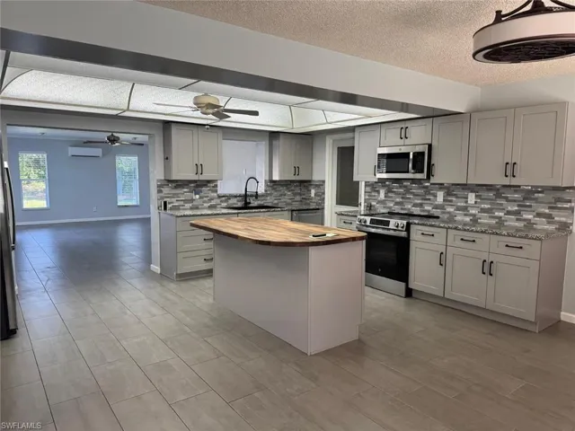 Kitchen with butcher block counters, gray cabinets, stainless steel appliances, backsplash, and a textured ceiling