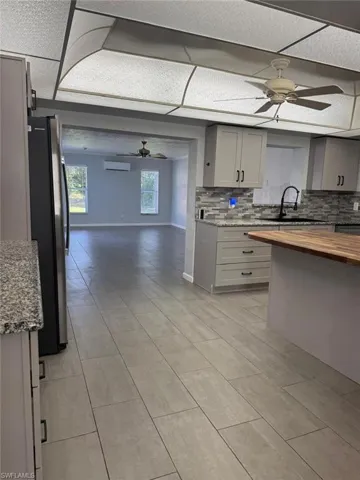 Kitchen with ceiling fan, open floor plan, gray cabinetry, decorative backsplash, and light stone counters