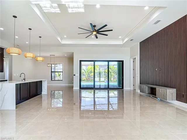 Living room with a tray ceiling, sink, ceiling fan, and light tile floors